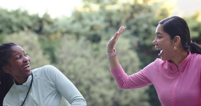 Diverse female friends following pink woman with watch, raising hand, helping friend stand in yard