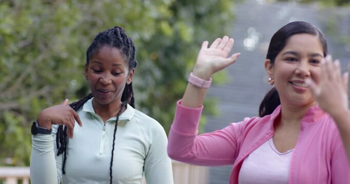 Diverse female friends greeting with high fives as pink jacket raising hand on deck with trackers