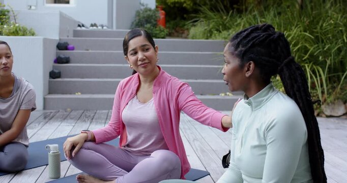 Diverse women on deck mats, right minttop speaking and seeking help, center in pink placing hand