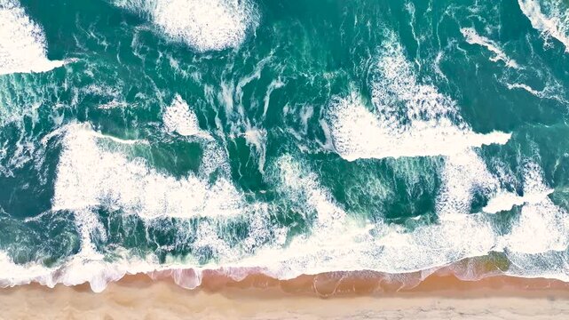 Ocean waves crash on sandy beach along the Atlantic coast of Portugal in summer with aerial perspective and clear blue sky