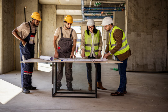 Construction team reviewing blueprint together inside unfinished building during renovation