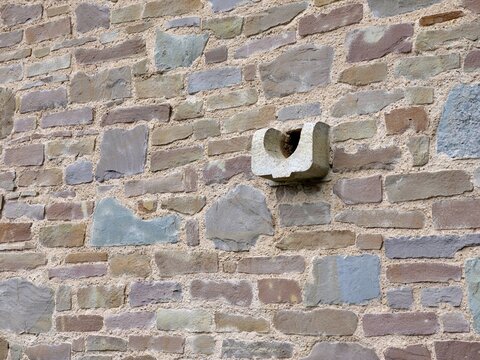 A medium shot focuses on a historic stone wall featuring a unique architectural
detail. The masonry is constructed from irregular, weathered blocks in shades of
brown, grey, and blue-grey with promine