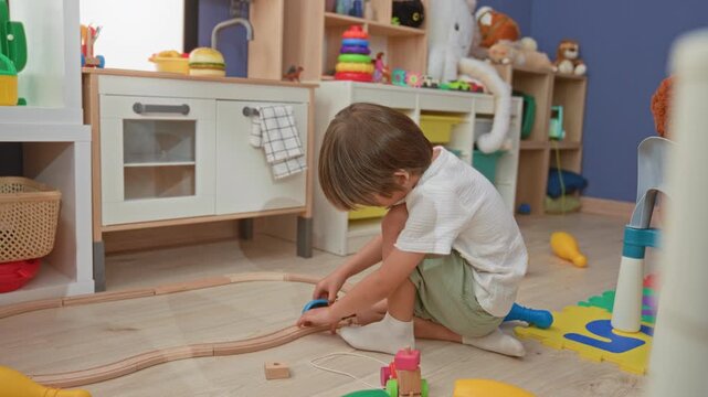 Boy kneeling, hands assembling wooden train track and toy car on floor in a playroom building; quiet concentration.