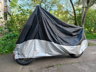 Black and gray nylon motorcycle cover protecting a parked motorbike in a quiet residential yard beside a multi story building © Harmony Video Pro