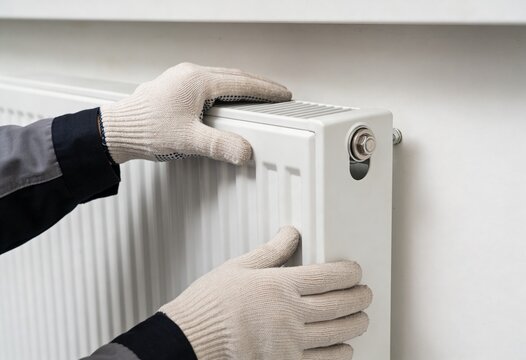 A close-up view of a professional worker in work gloves installing a modern white heating radiator.