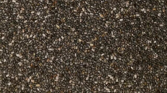 Top view macro shot of a heap of raw organic chia seeds rotating slowly. High quality background texture.
