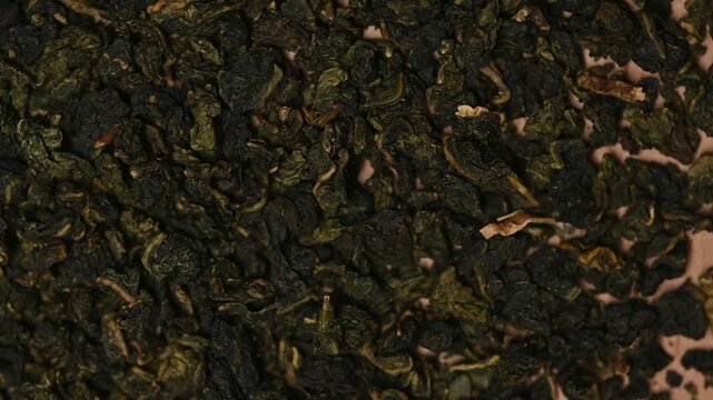 Top view macro shot of loose dried green tea 
leaves rotating slowly. Premium oolong tea texture background