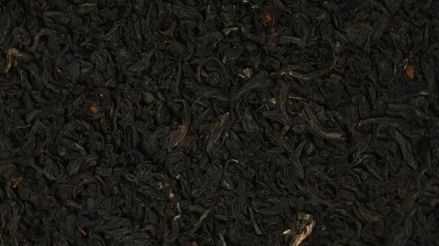 Macro top view shot of loose dried black tea leaves rotating slowly. Premium loose-leaf tea texture background.