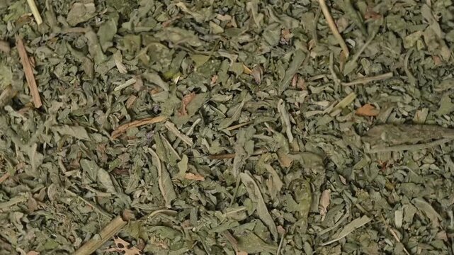 Top view macro shot of loose dried mint leaves rotating slowly. Premium organic peppermint or herbal tea ingredient texture background.