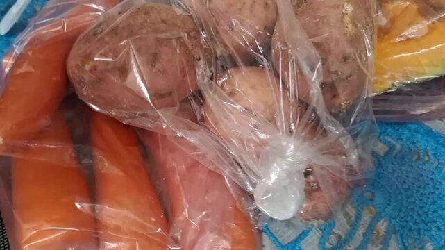 Fresh organic sweet potatoes and carrots inside clear plastic motion video