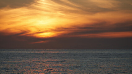 Obraz premium An orange-red sunset over the sea with the setting sun glinting on the calm water surface. Background image.