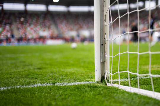 Close-up of a white soccer goalpost and net on a green grass pitch in a stadium background