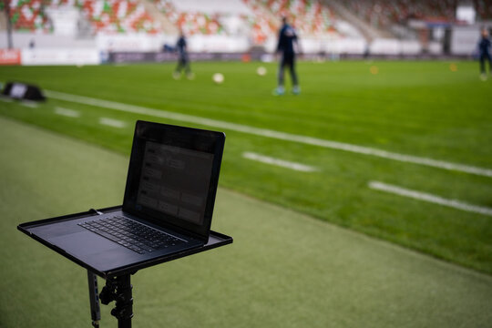 A laptop on a professional tripod stand positioned on the sidelines of a soccer pitch for data analysis during training