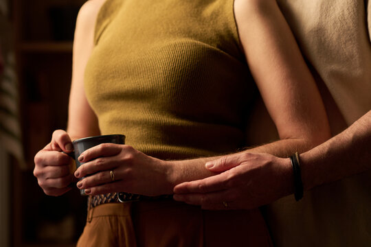 Close up of adult couple embracing while woman holding mug, showing intimacy, comfort, support in home setting. Ideal for relationship counseling, wellness, lifestyle marketing