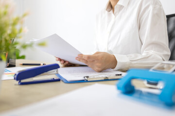Fototapeta premium Woman smiles while holding a blank document at her desk. Office supplies lie scattered around her workstation. Her expression shows calm focus and satisfaction 
