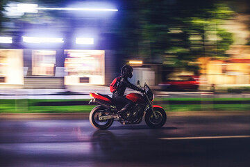 Fototapeta premium Motorcycle rider speeding through city at night