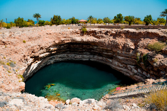 Hawiyat Najm sinkhole filled with emerald green water under a blue sky
