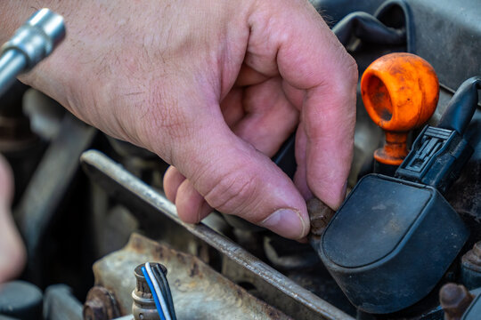 human hand carefully positions a small metal bolt onto an automotive ignition coil assembly while a socket wrench waits nearby during a routine engine maintenance task.