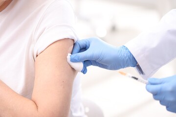 Fototapeta premium Doctor in medical gloves pressing patient's injection site after vaccination with cotton wool against blurred background, closeup