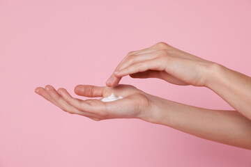 Fototapeta premium Woman applying hand cream on pink background, closeup. Space for text