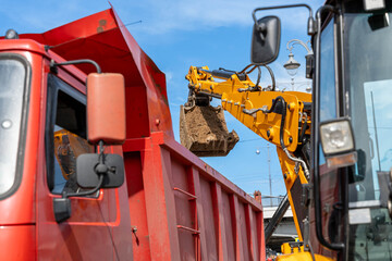 Rear Excavator Loading Red Dump Truck With Soil, Closeup Of Bucket Releasing Load, Bright Daylight, Operator Coordinating Haul, Heavy Transport © Egor Lint