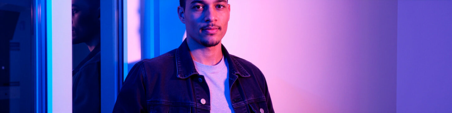 Portrait of young man standing near glass wall and looking at camera, conveying confidence and identity. Useful for branding, recruitment, lifestyle marketing, wide banner