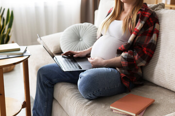 Obraz premium Pregnant woman working with laptop on sofa at home, closeup