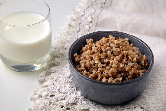 Cooked buckwheat groats in a ceramic bowl and a glass of milk on a linen tablecloth