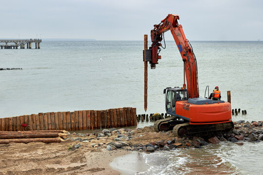Heavy construction equipment on the coastline. The machine drives piles from wooden logs to protect the beach from erosion