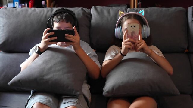 Two teenagers sitting on a sofa completely absorbed by their smartphones. Modern concept of technology addiction and alienation, screen time