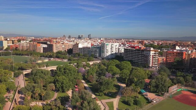 VALENCIA, SPAIN - MAY 27, 2026 Aerial view of the historic Saint Joseph Bridge crossing the Turia Gardens park, featuring lush green trees, sports fields, and the city skyline under a clear blue sky