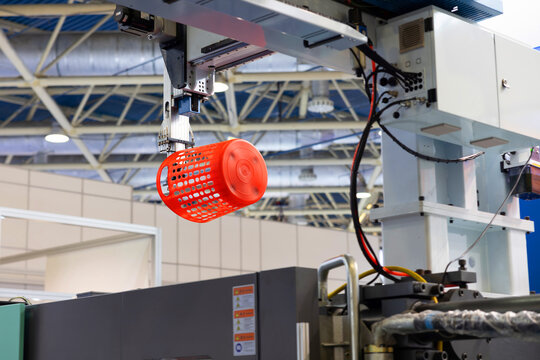 Automated process of molding plastic products on a CNC machine. The robotic arm of the machine moves the newly made red plastic basket. Injection molding of plastic objects