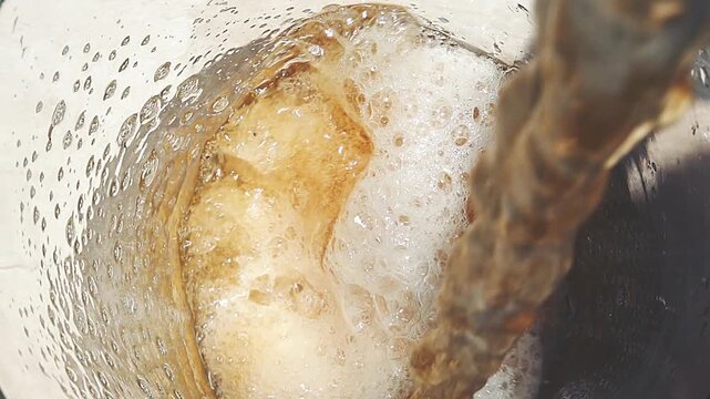 Overhead View of Cold Beer Pouring from Bottle into Glass Mug with Foam

