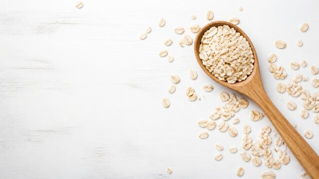 Wooden spoon holds oats on a white surface with scattered oats around the spoon showing the grains in detail