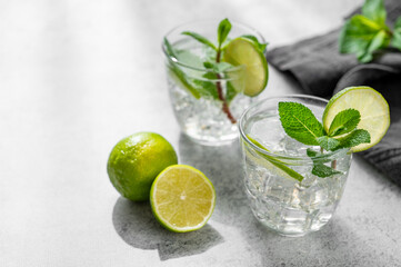 Fototapeta premium A fresh mojito with lime, mint and ice in glasses. Citrus lemonade or cocktail on a concrete background