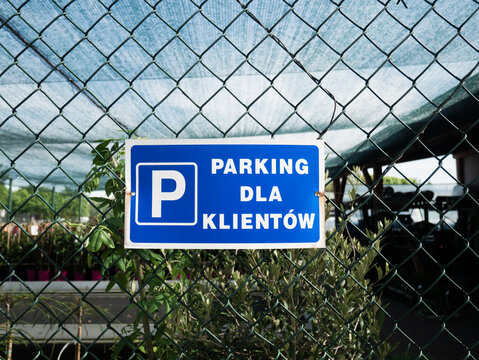 A blue sign with the inscription "Parking dla klient&oacute;w" attached to a metal chain-link fence in the city.