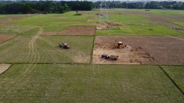 Aerial Drone Shot of Backhoe Loader Digging Soil and Loading Indian Tractor Trolley on Farmland. Excavator Loading Earth into Tractor Trailer in Agricultural Field.