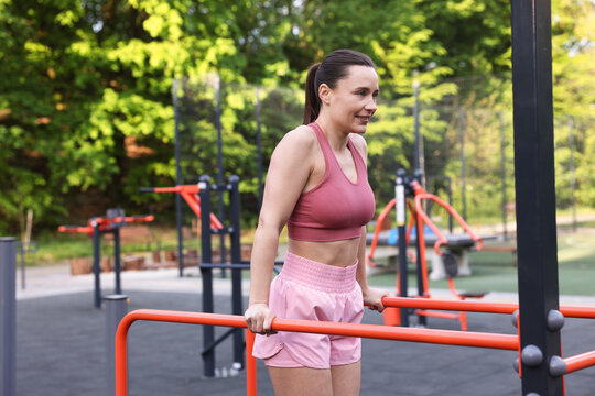 Athletic woman exercising on parallel bars at outdoor gym