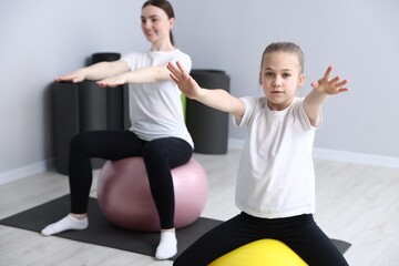 Fototapeta premium Little girl and trainer exercising with fitness balls indoors, selective focus