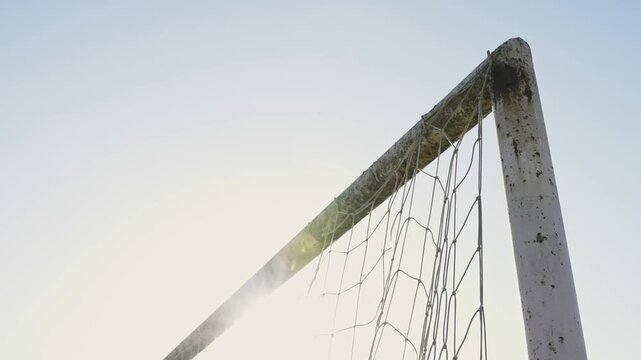 Close football scoring moment where the soccer ball hits the corner of the goal net. Player completes a shot during street football training. Rural field, childhood memories and competitive actions.