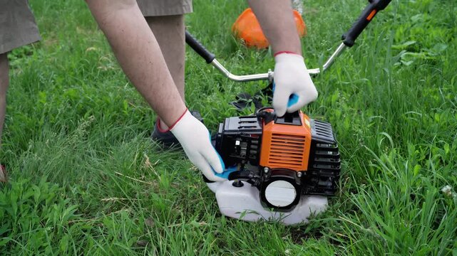 Individual in gloves adjusts the engine of a grass trimmer on a grassy lawn, showcasing a detailed view of the equipment and its components