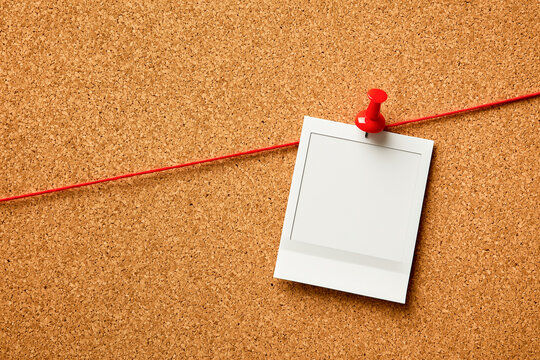 Blank instant photo frame pinned with a red pushpin and red string on a cork notice board. Detective investigation, mood board or memory mockup template