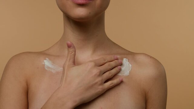 Cropped shot of Caucasian young woman gently applying body cream to collarbone area against solid studio background