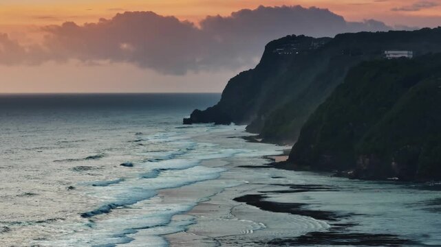 Melasti beach in Indonesia dramatic coastal cliffs meeting the rolling waves of the Indian Ocean, illuminated by the warm, subtle glow of a tropical low light sunset. Static shot nature panorama