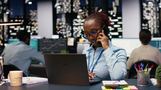 African american woman answering phone call for a briefing discussion, using laptop and requesting assistance. Manager does research on profitability, telephone call in office.