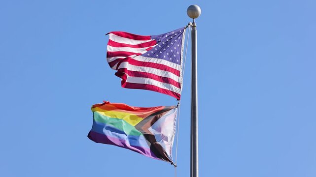 The US flag and the Progress Pride Flag blowing in the wind. Slow Motion.