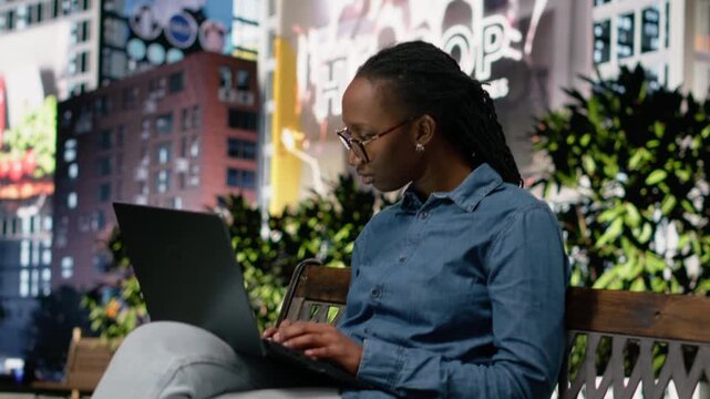 Happy black woman on park bench reading good news on laptop, feeling pleased after receiving excellent career upgrade and opportunity. Cheerful girl outside satisfied and in positive mood.