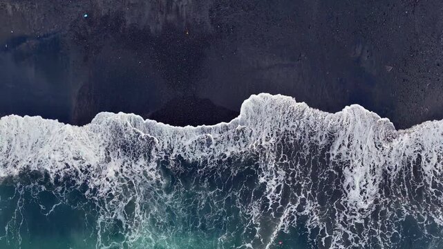 Aerial looking down at waves on a black sand beach in Bali Indonesia.