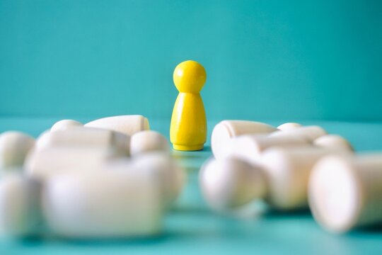 Low-angle, selective-focus shot of a yellow wooden peg doll standing amidst a background of fallen white figures, conceptualizing resilience, stability, or surviving a layoff.