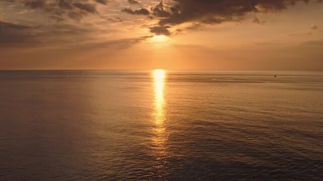 Golden sunset light reflecting on calm sea creating dazzling light ray across the water, with a few faint boats on the horizon in Phuket, Thailand. Tropical nature background. Aerial view drone flight